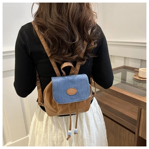 Mini brown leather and blue denim backpack worn by a model in a cozy interior setting