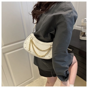 Close-up of white crocodile pattern crescent bag with golden chain and metal studs