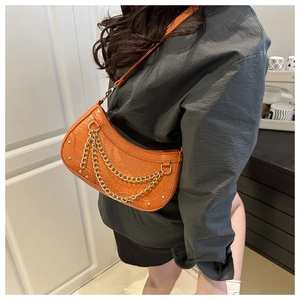 Detail of orange crocodile embossed underarm bag with gold metal chains and rivets