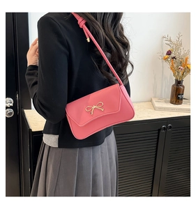 Gros plan d'un sac porté épaule rose avec boucle nœud dorée sur fond minimaliste chic