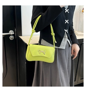 Close-up of bright green handbag featuring a delicate golden bow clasp and glossy finish