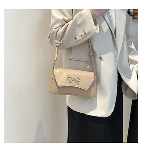 Detail of a beige baguette bag with a gold metal bow and smooth PU leather finish