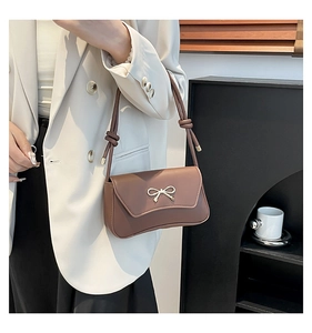 Détail d'un sac porté épaule marron avec un nœud métallique et une bandoulière nouée