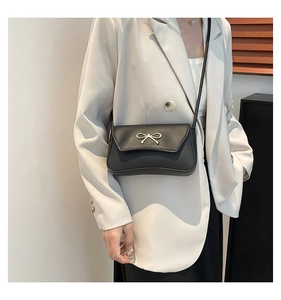Détail du sac à main noir minimaliste avec boucle de nœud dorée sur costume crème