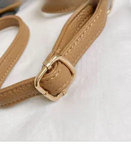Detail of a brown leather shoulder strap featuring a gold square metal adjustment buckle