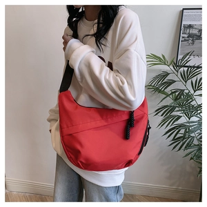 Detail of red crescent bag featuring black adjustable strap and woven zipper pullers