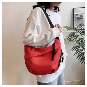 Close-up of a red semi-circular crossbody bag with black wide strap and woven zipper detail