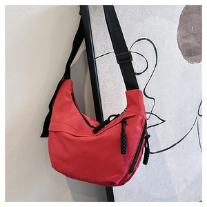 Detail of red crescent shoulder bag with black woven zipper pulls and wide strap