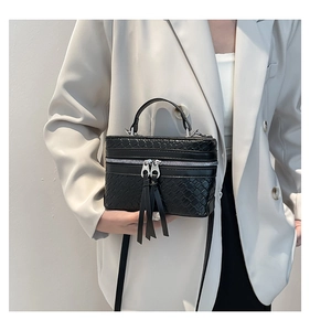 Detail of black woven box handbag featuring silver zippers and long fringe tassels