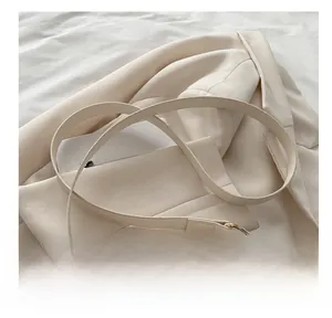 Gros plan du sac bandoulière en cuir crème avec boucle dorée sur un blazer blanc
