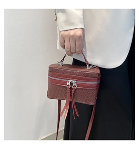 Detail of burgundy box bag with woven texture, metal zippers, and top handle being held