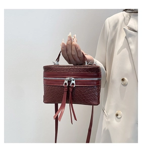 Close-up of a burgundy woven box bag with dual metal zippers and long leather pullers