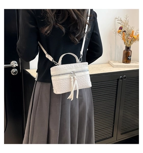 Detail of white woven bucket bag featuring elegant tassel zipper and leather top handle