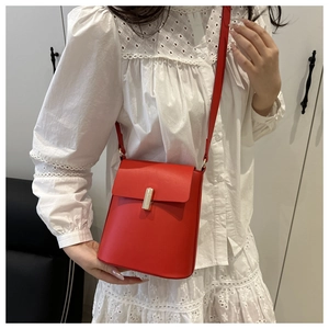 Détail d'un sac seau rouge en cuir mat avec un fermoir métallique rectangulaire doré