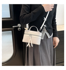 Detail showing white bucket bag with woven texture, bow accents and double zippers