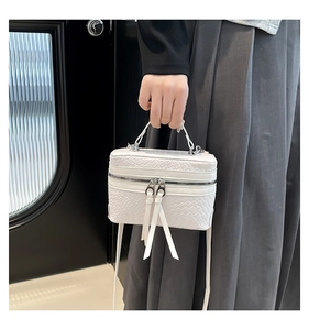 Close-up of white woven leather box bag showing silver double zippers and textured surface