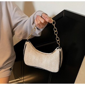 Détail d'un sac demi-lune en paille tressée avec liseré noir et chaîne dorée
