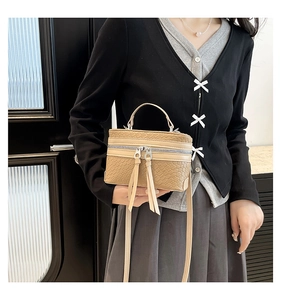 Detail of beige box bag showing woven texture and long decorative tassels on the zippers