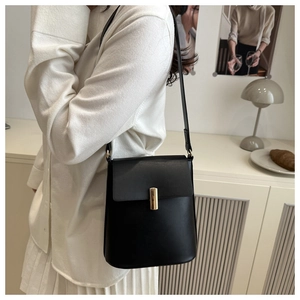 Détail d'un sac bandoulière en cuir noir avec boucle dorée porté par un mannequin