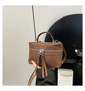 Détail d'un sac boîte marron tressé avec double fermeture éclair dorée et longs glands