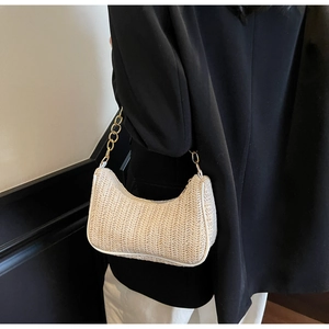 Détail du sac demi-lune en paille tressée avec bordure en cuir blanc porté par le mannequin