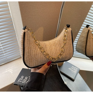 Détail du sac baguette en paille avec bordure en cuir noir et bandoulière chaîne dorée