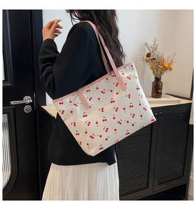 Detail of a large white tote bag with red cherry prints and pink leather handles