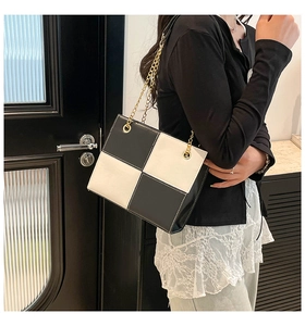 Detail of black and white checkerboard PU leather bag with elegant gold chain strap