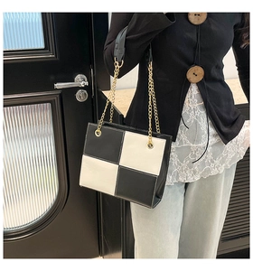 Detail of checkered leather tote bag with gold chain strap on a stylish model