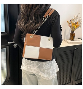 Detail of checkered brown and white shoulder bag with gold chain strap on model