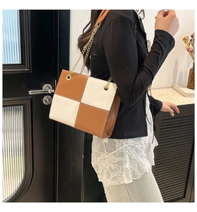 Detail of checkered brown and white shoulder bag with thin gold chain strap on model