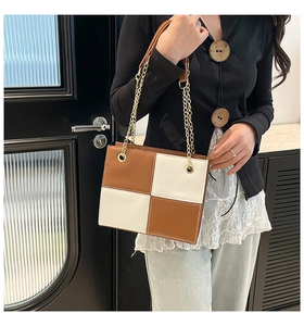 Detail of a brown and white color-block crossbody bag with a gold chain strap