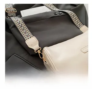 Detail of golden metal hooks and geometric woven strap on a cream leather pillow bag