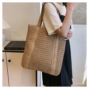 Detail of hand-woven straw tote bag showing intricate natural fiber texture and wide handle