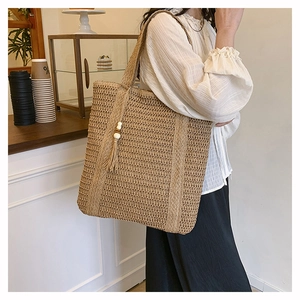 Detailed texture of woven straw tote bag featuring decorative fringe and wooden beads