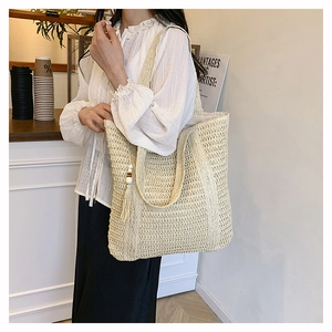 Close-up of beige woven tote bag with bohemian tassel and wooden bead charm detail