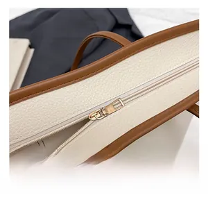 Detailed close-up of beige lychee leather texture and golden metal zipper on tote bag