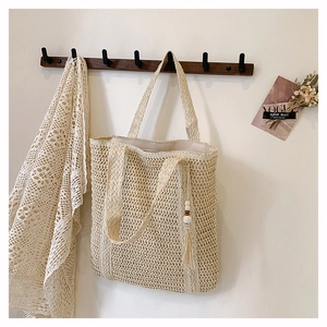 Close-up of hollow straw tote bag with woven handles and decorative wooden bead tassels