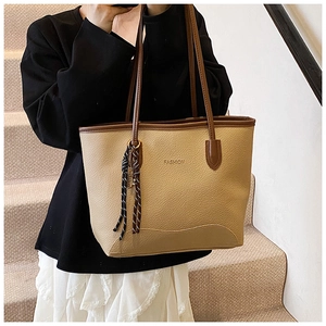 Detail of beige litchi grain tote bag with brown handles and woven pendant