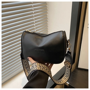 Close-up of black crossbody bag with embossed fashion text and geometric woven wide strap