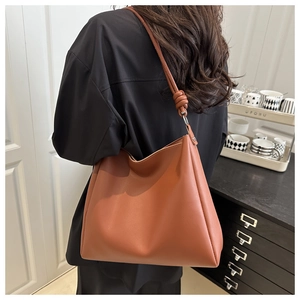 Close-up of caramel leather bucket bag featuring unique knot detail on shoulder strap