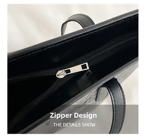 Detail showing smooth silver metal zipper and crocodile embossed texture on black tote bag