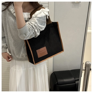 Detail of black corduroy tote bag showing vertical rib texture and leather piping trim