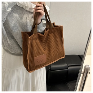 Detail of brown corduroy tote bag featuring a leather fashion patch and thick straps