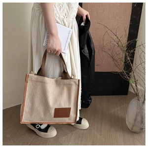 Detailed close-up of beige corduroy tote bag featuring brown canvas handles and leather patch