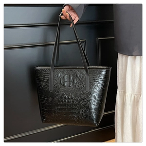 Detail of black crocodile embossed tote bag with glossy finish and slim shoulder straps