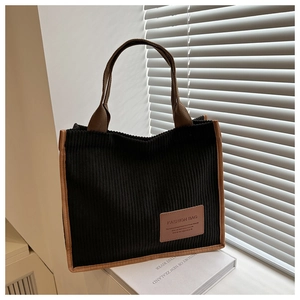 Detailed close-up of black corduroy tote bag with brown straps and leather fashion label