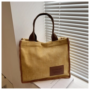 Detail of yellow corduroy tote bag with brown straps and faux leather patch