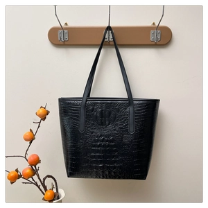 Detail of black crocodile embossed tote bag hanging on wooden hook with persimmon branch