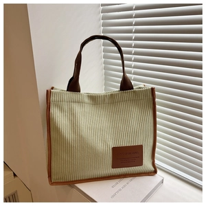 Close-up of light green corduroy tote bag with brown leather patch and woven handles
